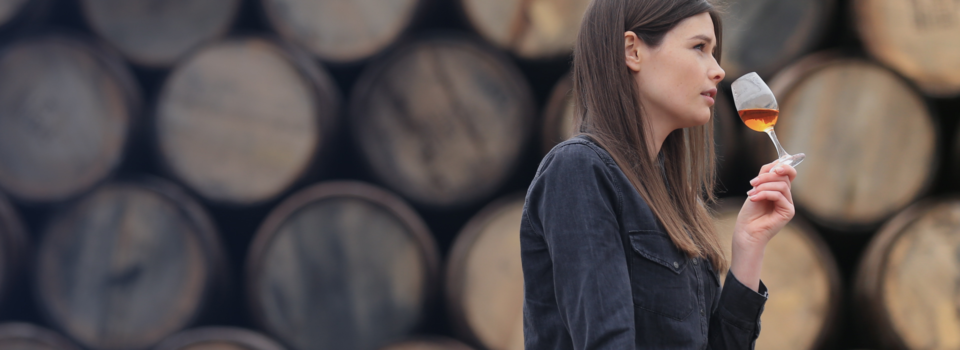 Woman standing in front of whisky barrels drinking a shot of whisky